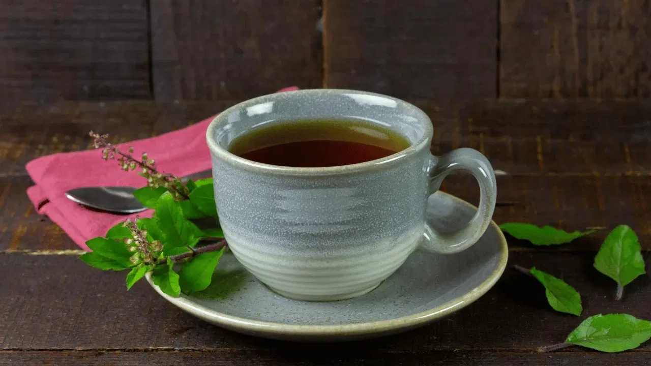 Fresh tulsi leaves and warm tulsi water in a glass